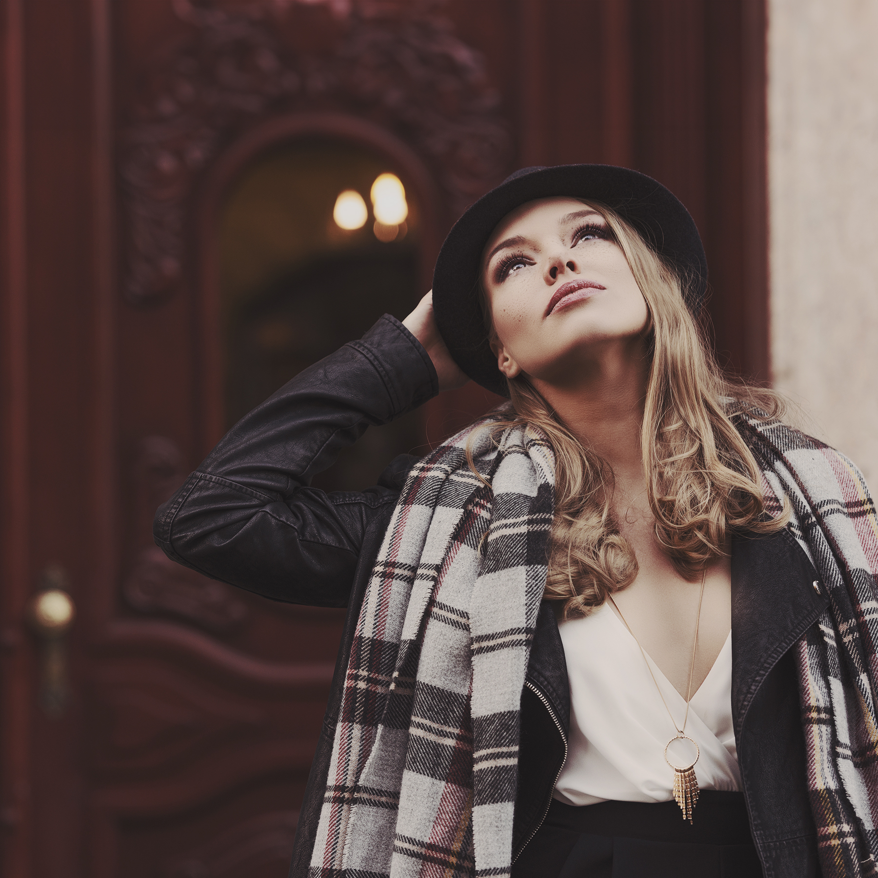 fashion shot of pretty young woman near e old fashion door she is looking up to the sky wearing scarf and hat . freckles on face